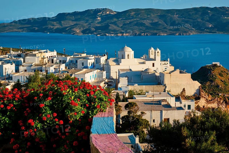 Picturesque scenic view of Greek town Plaka on Milos island over red geranium flowers and Orthodox greek church