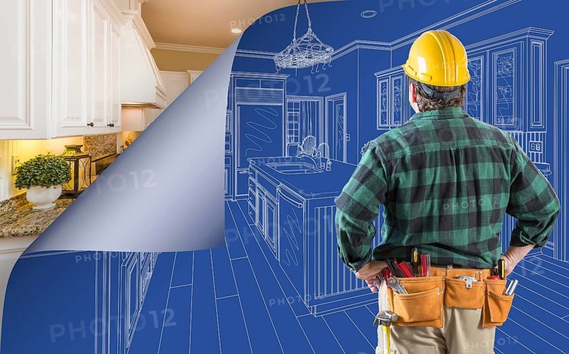 Contractor standing in front custom kitchen blueprint drawing with page corner curling to reveal finished construction