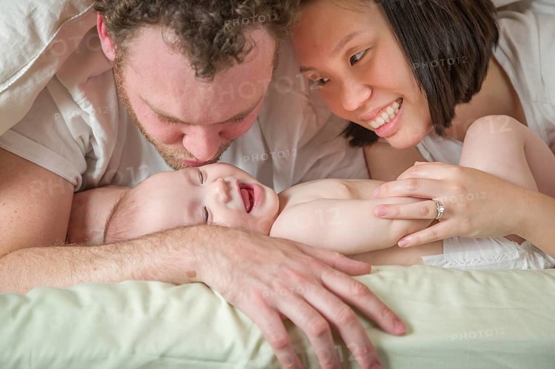 mixed-race chinese and caucasian baby boy laying in bed with his father and mother