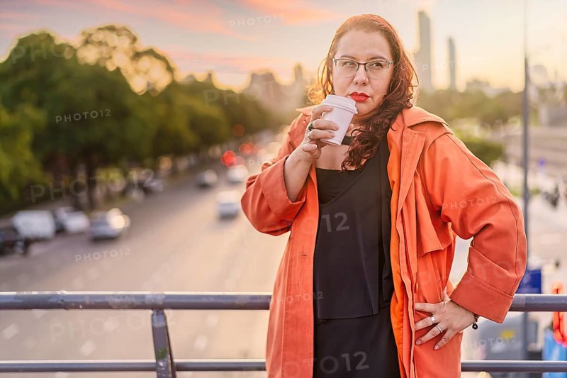 Woman standing on a bridge at sunset having a coffee
