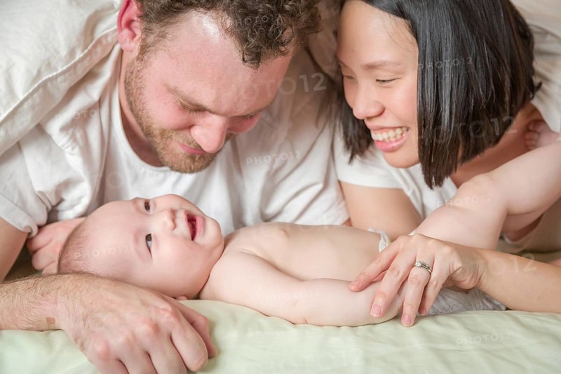 mixed-race chinese and caucasian baby boy laying in bed with his father and mother