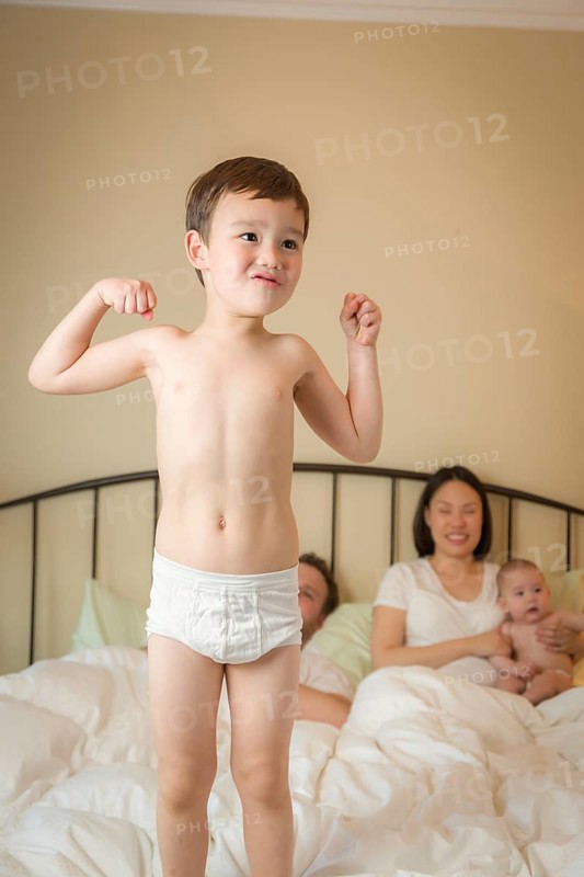 Young mixed-race chinese and caucasian boy jumping in bed with his family