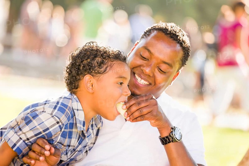 African american father and mixed-race son eating an apple in the park