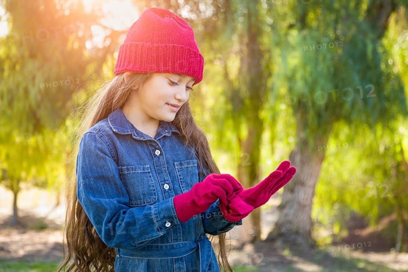 Cute mixed-race young girl wearing red knit cap putting on mittens outdoors