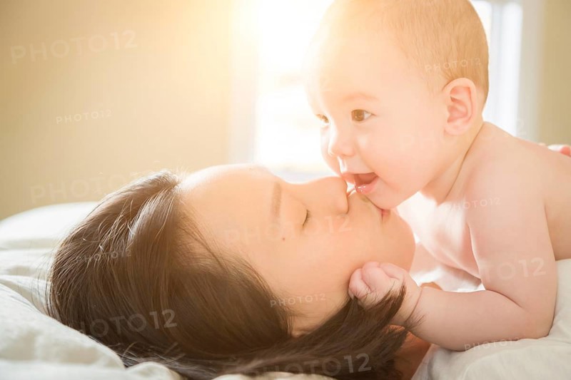 Young mixed-race chinese and caucasian baby boy laying in his bed with his mother