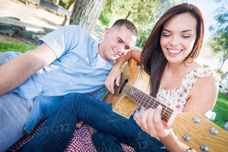 Young adult girl playing guitar with boyfriend in the park