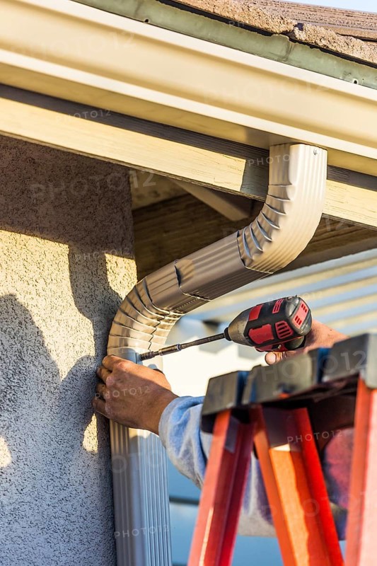 Worker attaching aluminum rain gutter and down spout to fascia of house