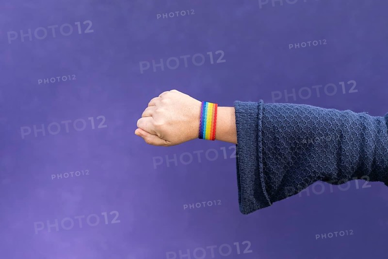 Detail of arm and hand of woman wearing gay wristband on purple background