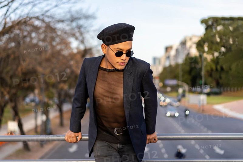 Latino gay male with makeup wearing trendy hat posing on a bridge