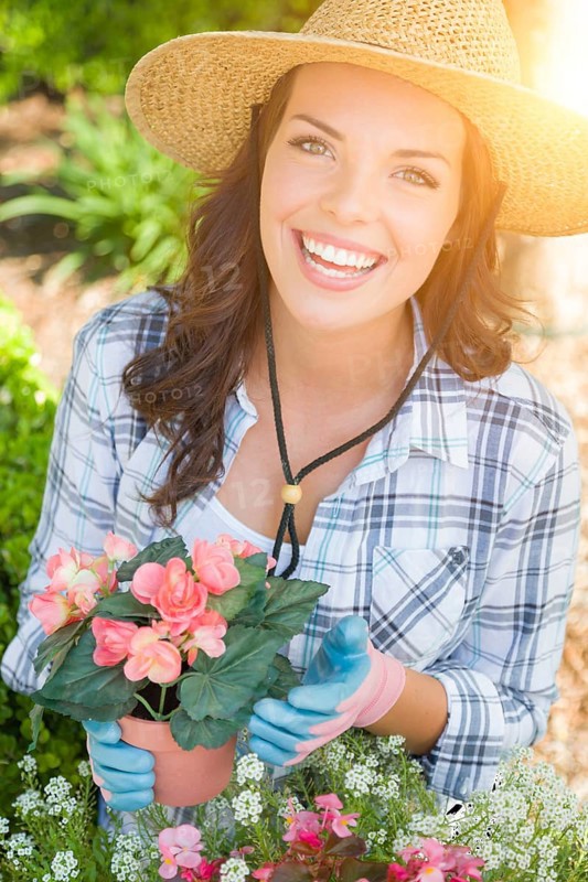 Happy young adult woman wearing hat and gloves gardening outdoors