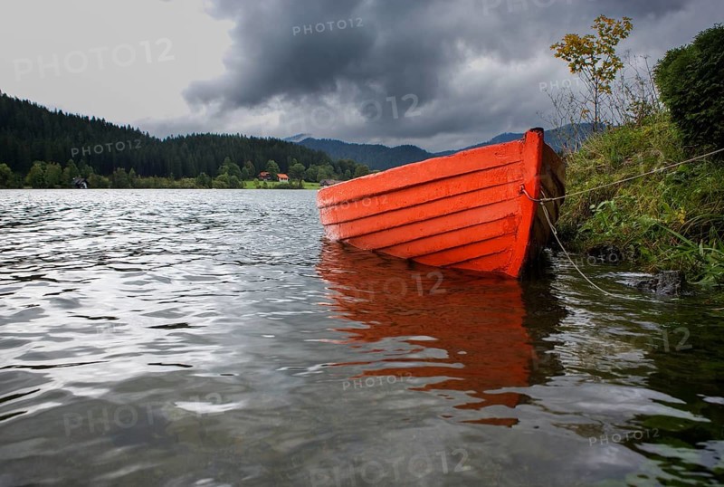 Leeres rote Ruderboot am Seeufer bei Regenwetter