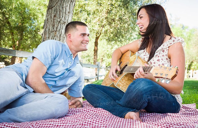 Young adult girl playing guitar with boyfriend in the park