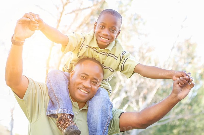 Happy african american father and son riding piggyback outdoors at the park