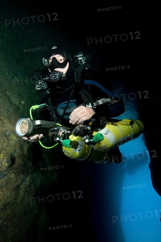 Diver dives into entrance of underwater cave with special equipment Diving equipment for cave divers