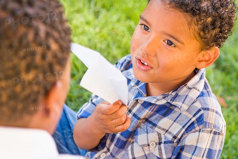 Happy african american father and mixed-race son playing with paper airplanes in the park