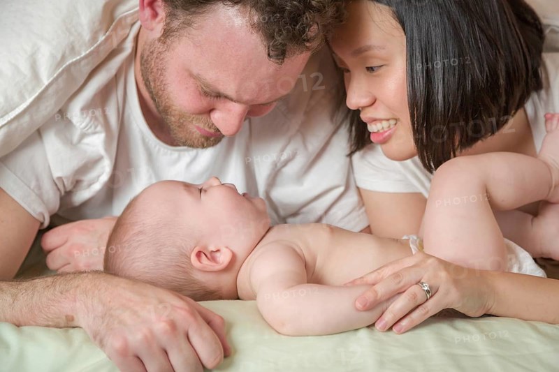 mixed-race chinese and caucasian baby boy laying in bed with his father and mother