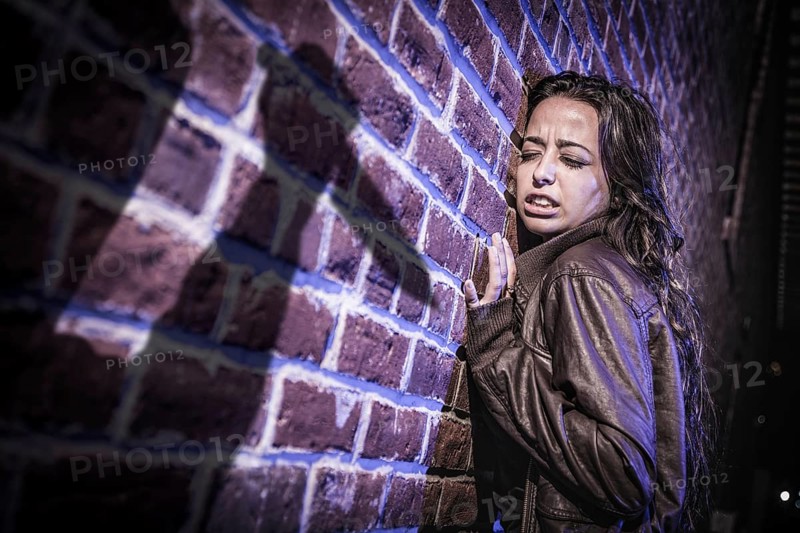 Male shadow figure with knife threatens frightened young woman against brick wall