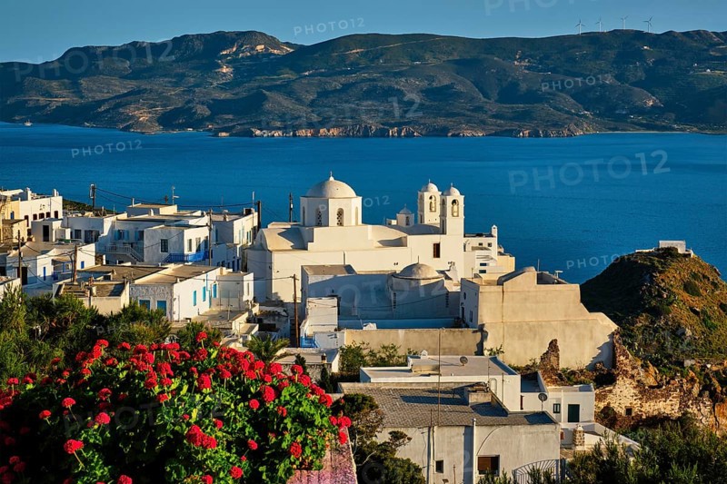 Picturesque scenic view of Greek town Plaka on Milos island over red geranium flowers and Orthodox greek church
