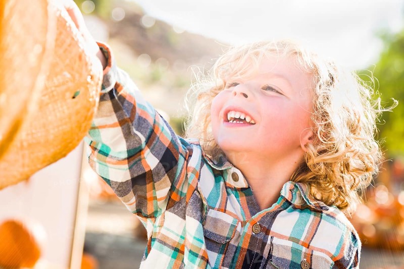 Little boy sitting with A cowboy hat in a rustic ranch setting at the pumpkin patch
