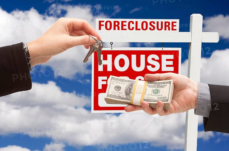 Handing over cash for house keys in front of foreclosure sign and cloudy blue sky