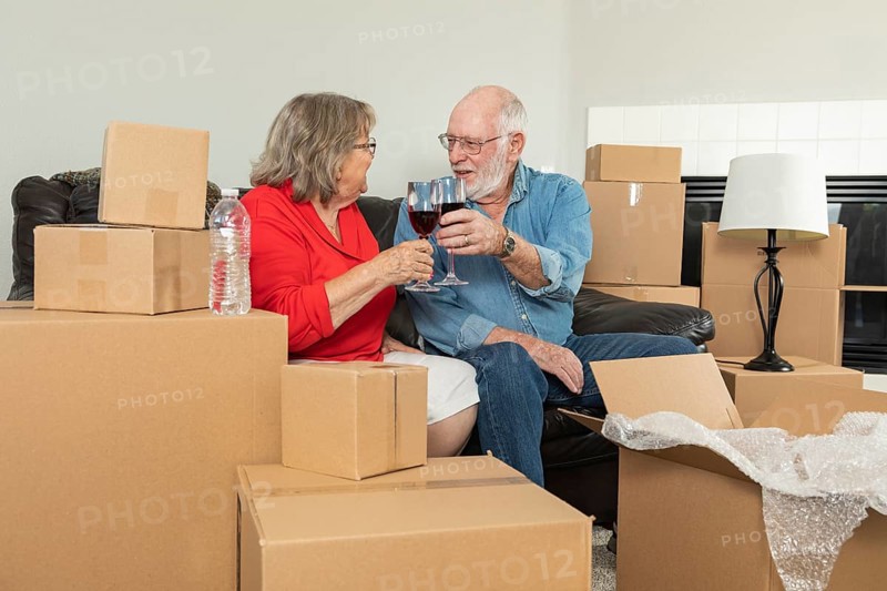 Senior adult couple toasting wine glasses surrounded by moving boxes