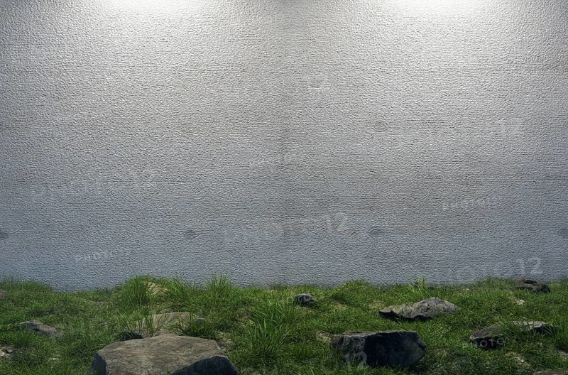 Mysterious blank cement wall surrounded by large rocks and grass in field