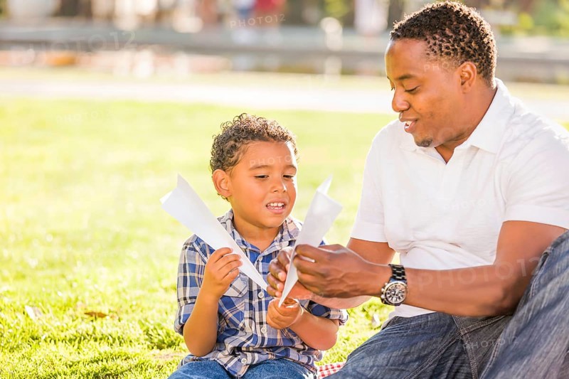Happy african american father and mixed-race son playing with paper airplanes in the park