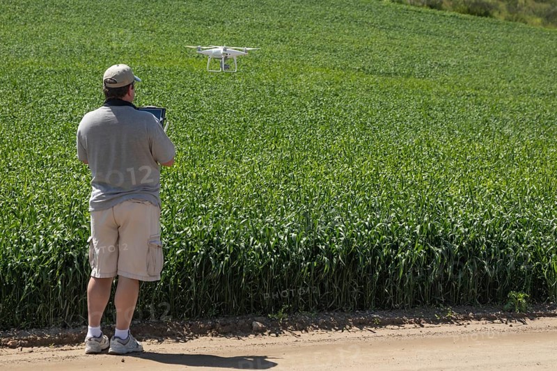 Pilot flying unmanned aircraft drone gathering data over country farmland field