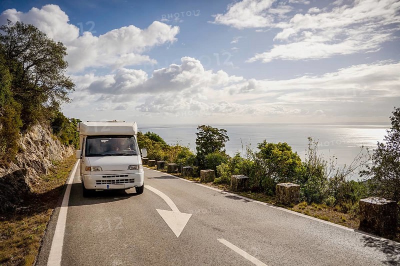 Small camper van driving on scenic road with sea views in Arrabida Natural Park