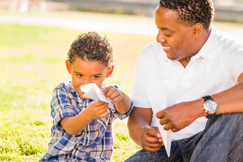 Happy african american father and mixed-race son playing with paper airplanes in the park