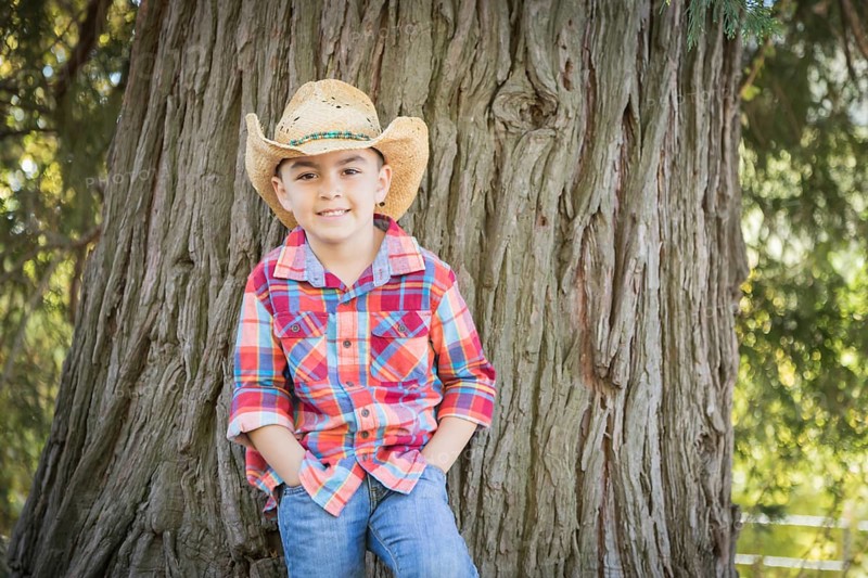 mixed-race young boy wearing cowboy hat standing outdoors