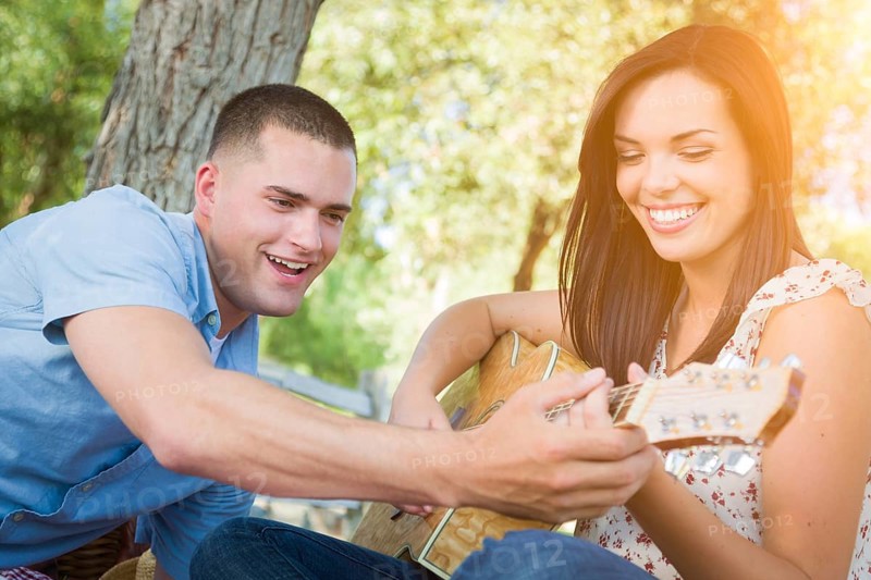 Handsome young man teaching mixed-race girl to play guitar at the park