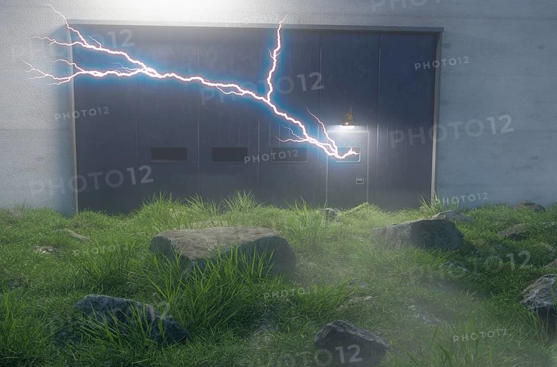 Lighting charge coming from cement wall and iron door with windows surrounded by large rocks in field