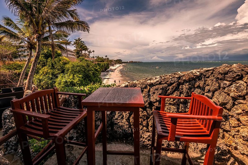 A view over two chairs with a table onto a beach and the sea. Sunset on the Indian Ocean