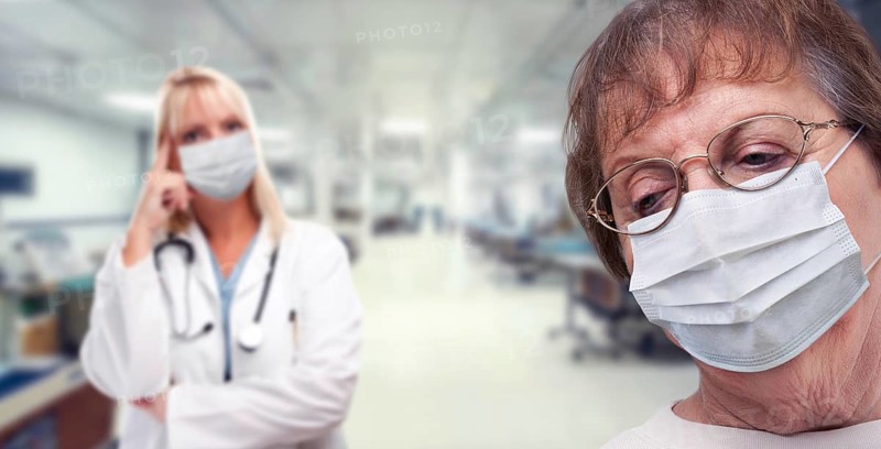 Senior adult female looking down as doctor stands behind all wearing medical face masks within hospital