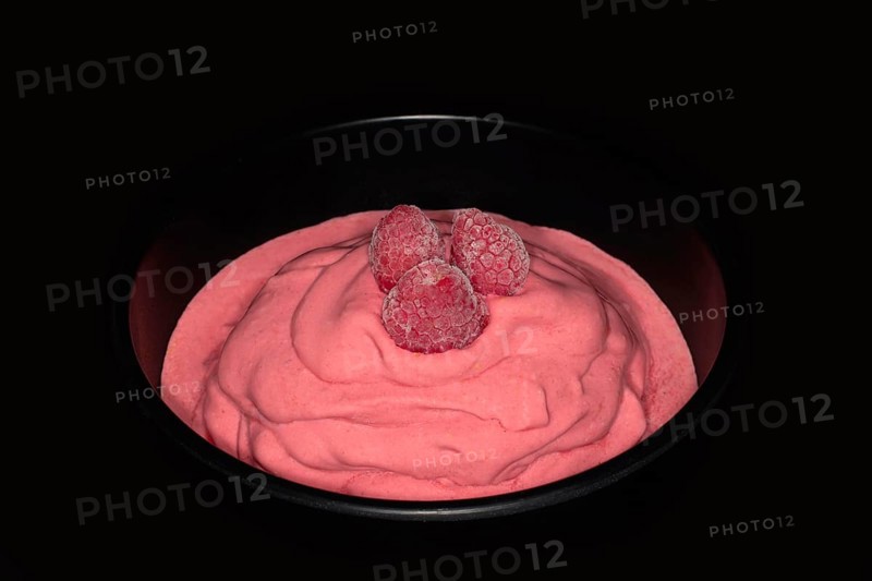 Three frozen raspberries on a raspberry ice cream in a black porcelain bowl