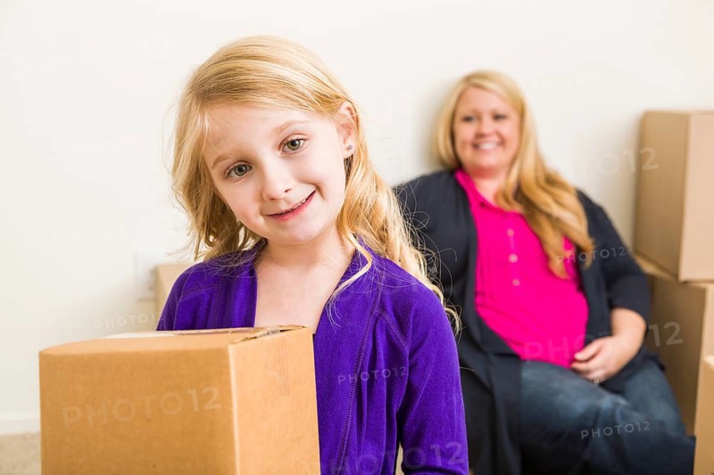 Happy young mother and daughter in empty room with moving boxes