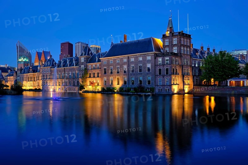 View of the Binnenhof House of Parliament and the Hofvijver lake with downtown skyscrapers in background illuminated in the evening