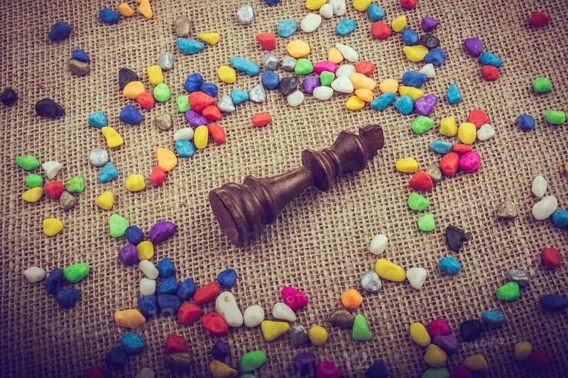 Chess king amid colorful pebbles on canvas background