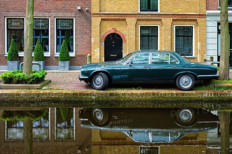 Old black retro car on canal embankment in street of Delft with reflection. Delft