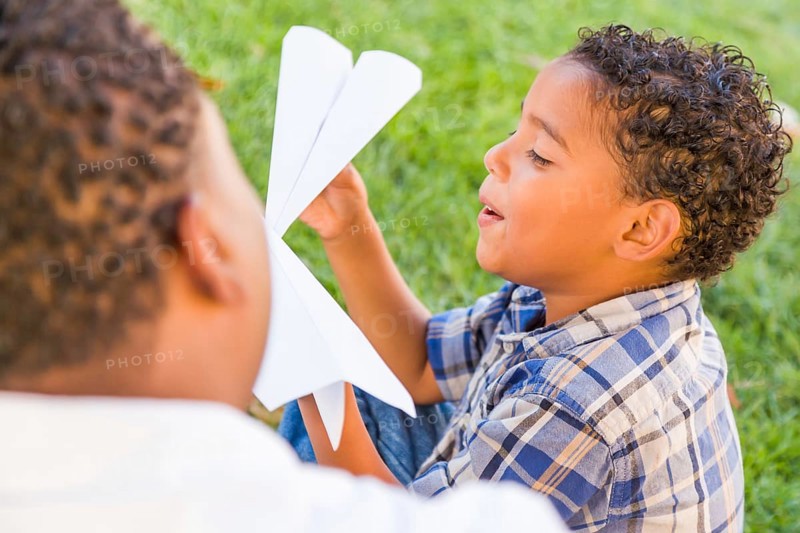 Happy african american father and mixed-race son playing with paper airplanes in the park