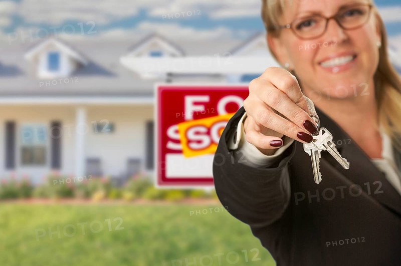 Real estate agent handing over new house keys with sold sign behind