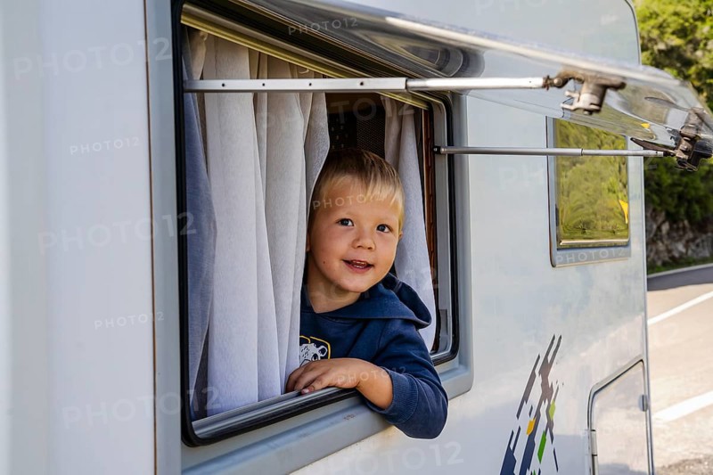 Happy small boy looking through the RV's window parked along the road
