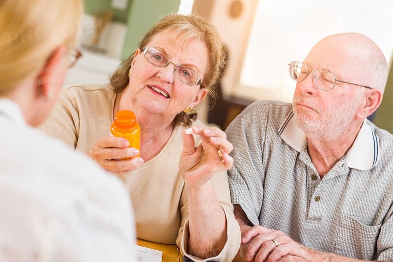 Doctor or nurse explaining prescription medicine to senior adult couple