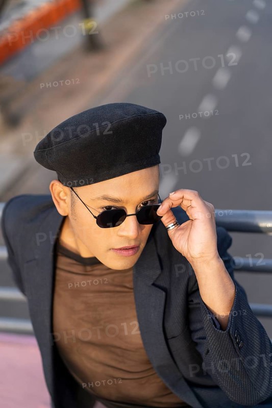 Latino gay male with makeup wearing trendy hat posing on a bridge