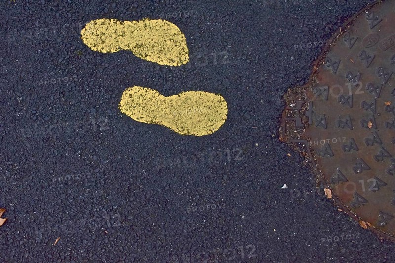 Two yellow footprints in the asphalt in front of manhole cover