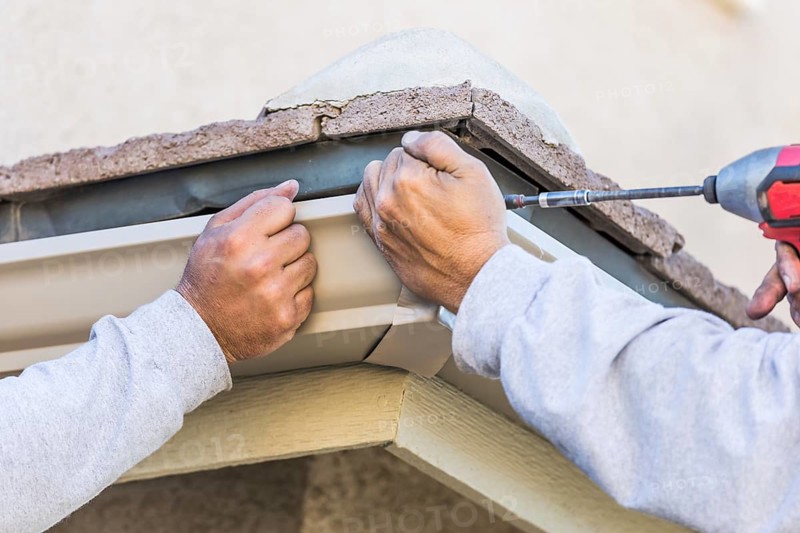 Workers attaching aluminum rain gutter to fascia of house