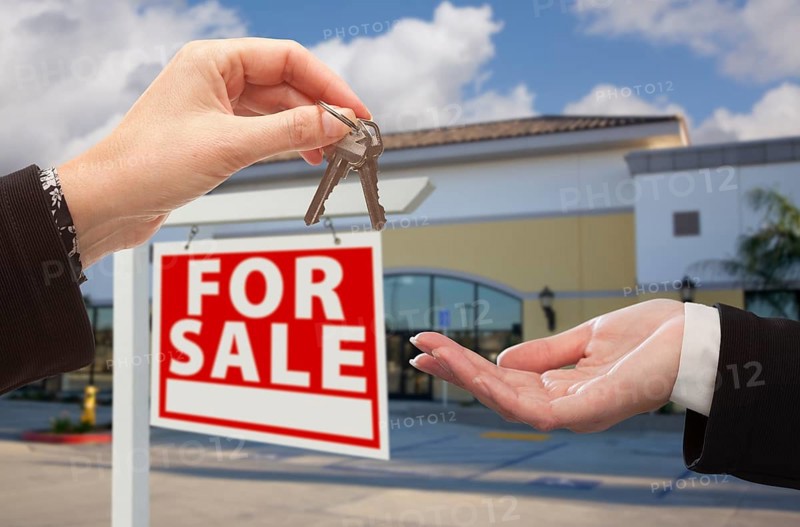 Real estate agent handing over the keys in front of vacant business office and for sale sign