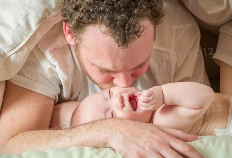mixed-race chinese and caucasian baby boy laying in bed with his parents