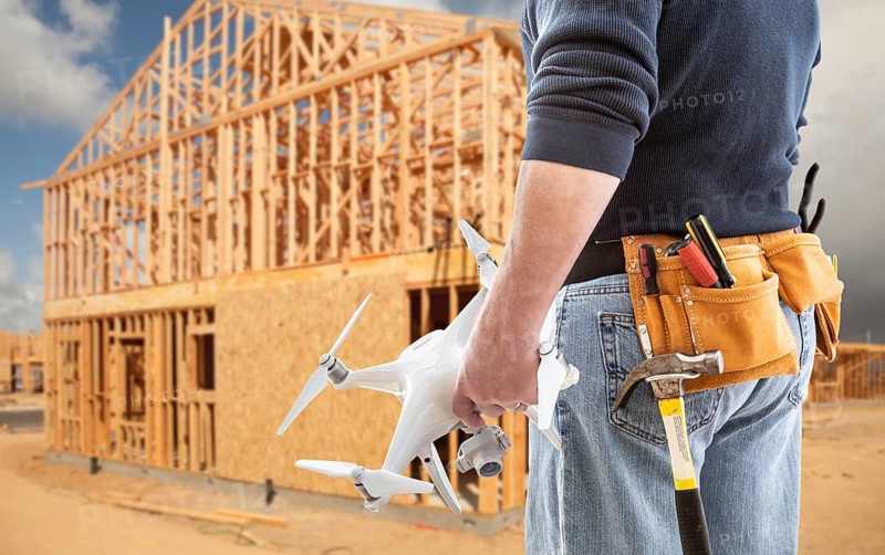 Construction worker and drone pilot with toolbelt holding drone at construction site